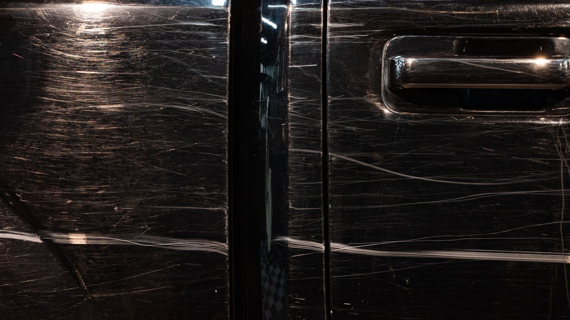 The same black door before correction, covered in swirl marks and scratches