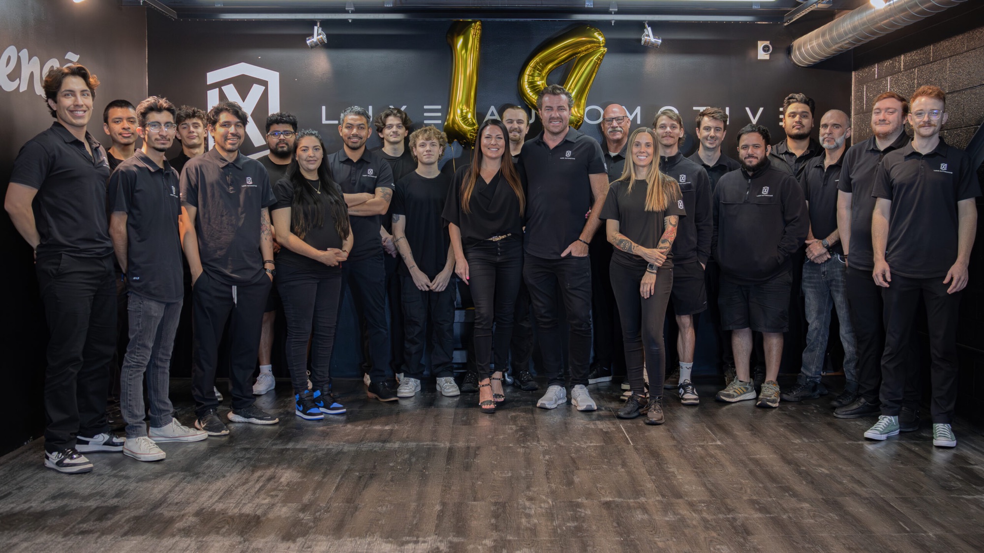 The whole LUXE Automotive team beneath the brand wall at the fourteenth anniversary