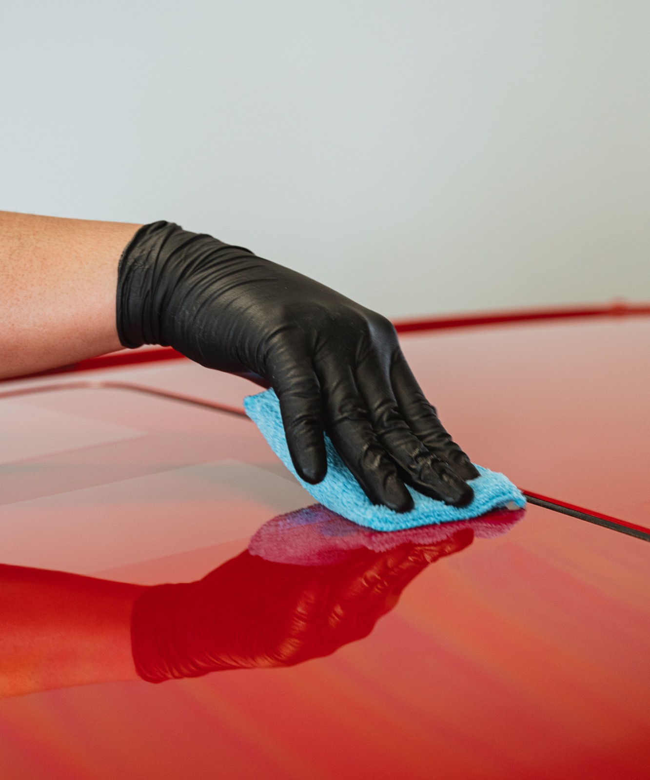 A gloved hand applying ceramic coating to red paint